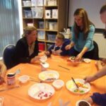 teachers and pupils sitting at a table with one adult serving food