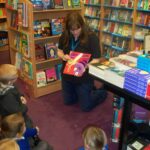 Teacher kneeling on floor showing pupils a book in the library