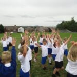 pupils outside in gym clothes doing exercises with their hands in the air