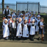 group of pupils dressed in victorian costume standing in front of school gates
