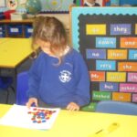 pupil standing at a desk counting coloured buttons in fornt of a school display board