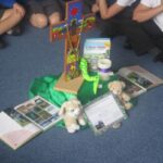 pipils sitting on floor staring ata collection of items including a cross, stuffed toy and photographs