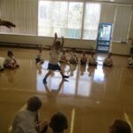 pupils all sitting on the gym floor watching a pupil perform with a hula hoop