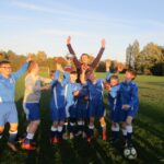 pupils in blue football strips all celebrating with hands in the air and holding a trophy