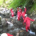 pupils in red waterproofs and helmets walking in a stream up a rugged hill